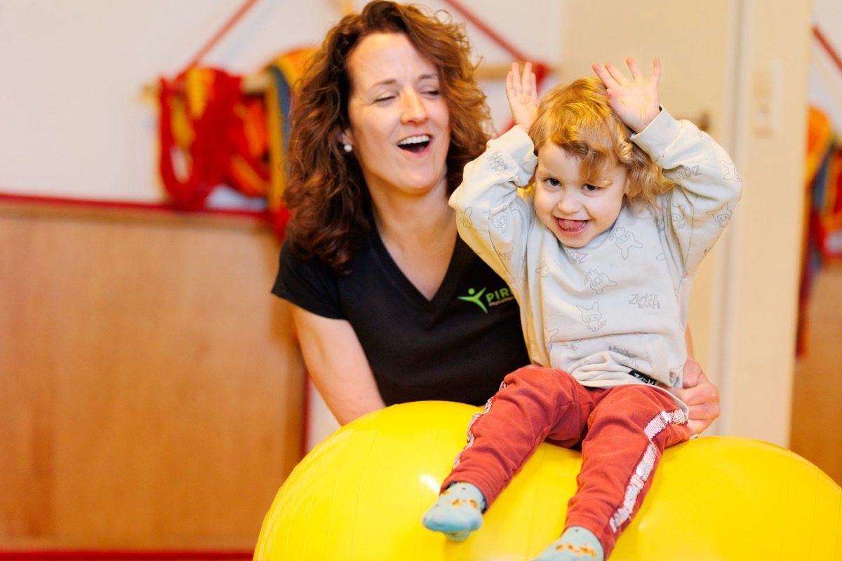 Therapeutin unterstützt ein Kind beim Sitzen auf einem Therapieball